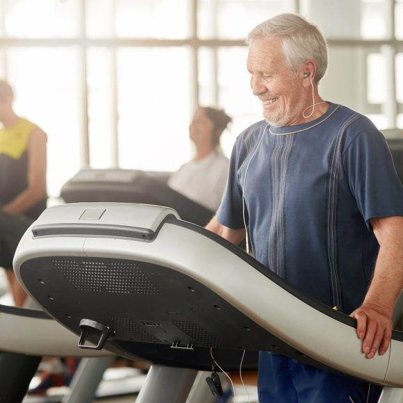 Smiling senior man on treadmill at gym. Male pensioner exercising at fitness club. Morning workout at gym.